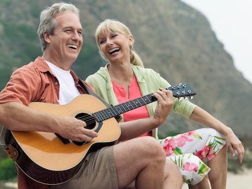 man playing guitar while woman smiling on Kauai beach